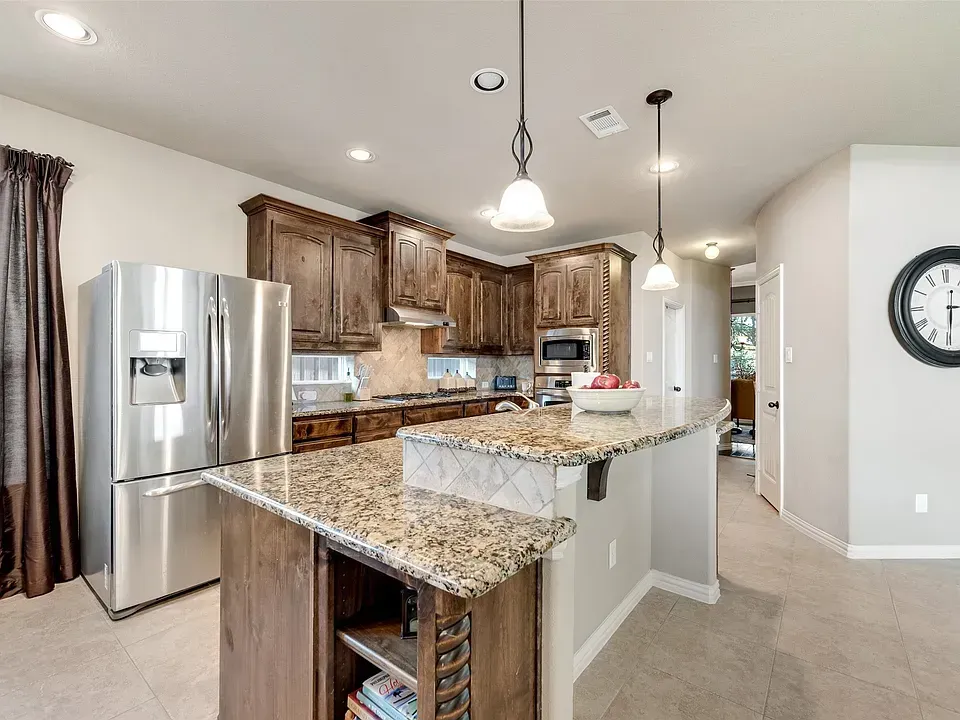 Modern kitchen with granite island, stainless steel refrigerator, wood cabinets, and pendant lights