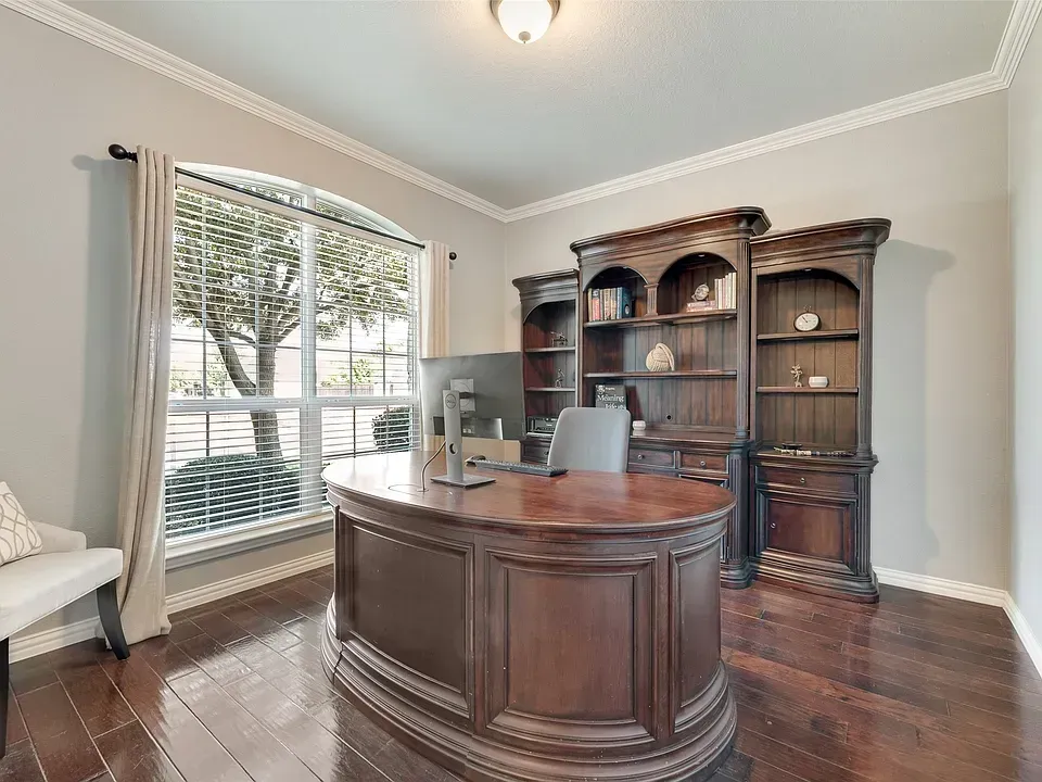Elegant home office with dark wood desk, bookcase, and window with blinds on hardwood floors