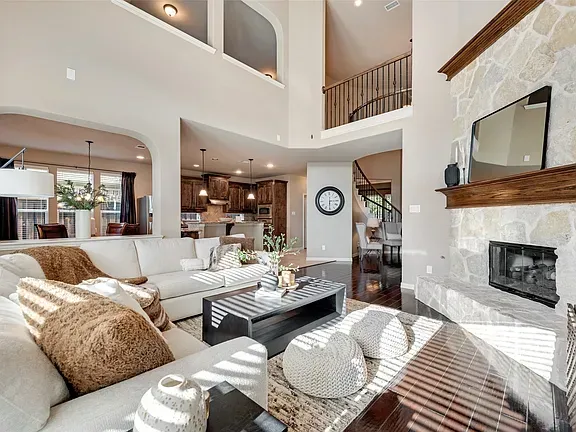 Bright living room with white sofas, fireplace, and vaulted ceiling overlooking a kitchen and loft.