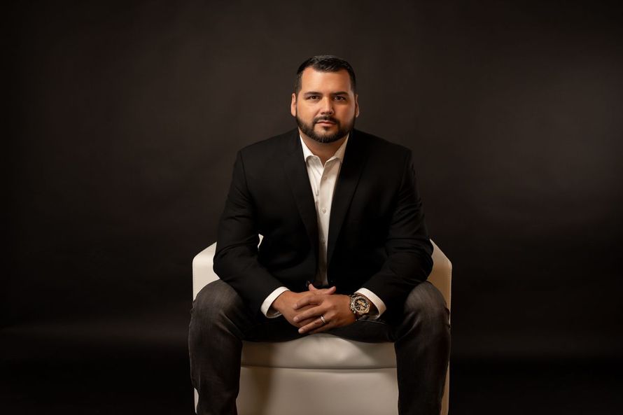 A man in a suit is sitting in a chair with his hands folded.
