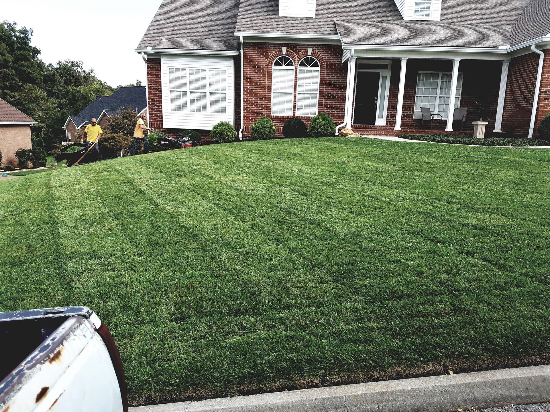 A truck is parked in front of a brick house with a lush green lawn.