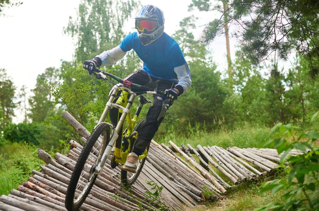 Mountain biker in blue riding down a wooden ramp in a forest.