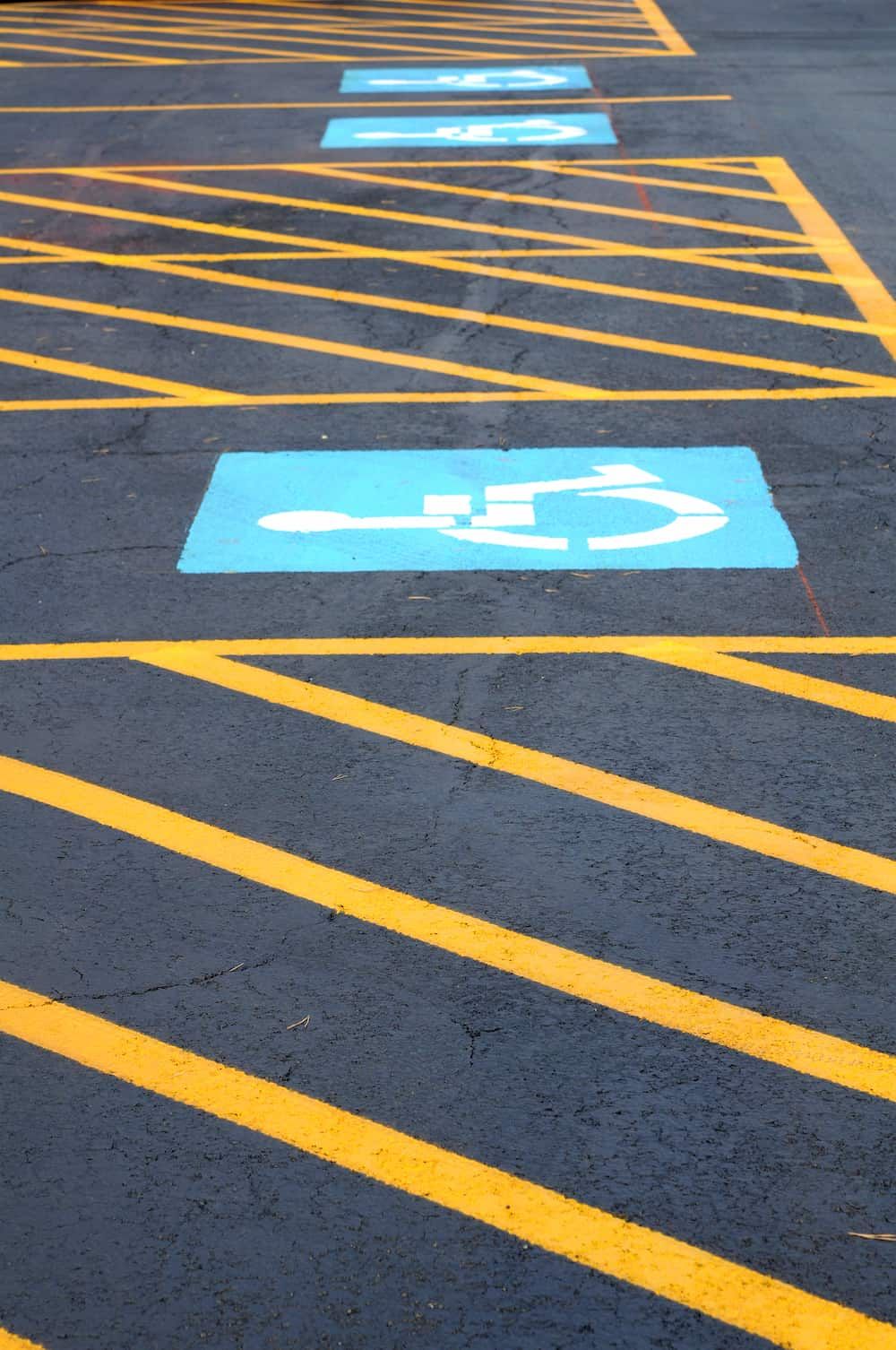 Blue handicap parking spaces with white wheelchair symbols, marked by yellow diagonal stripes on asphalt.