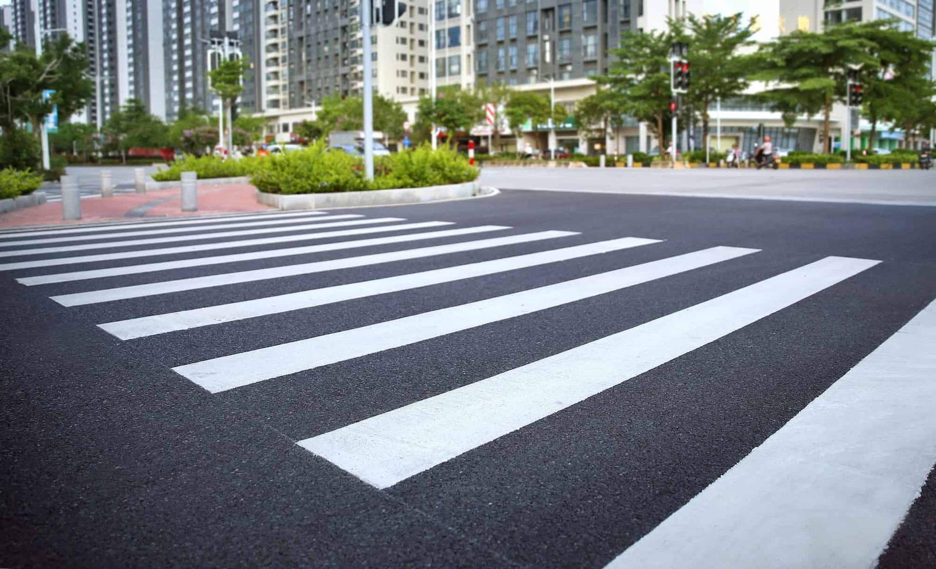 Crosswalk on asphalt road with buildings in the background and green trees.