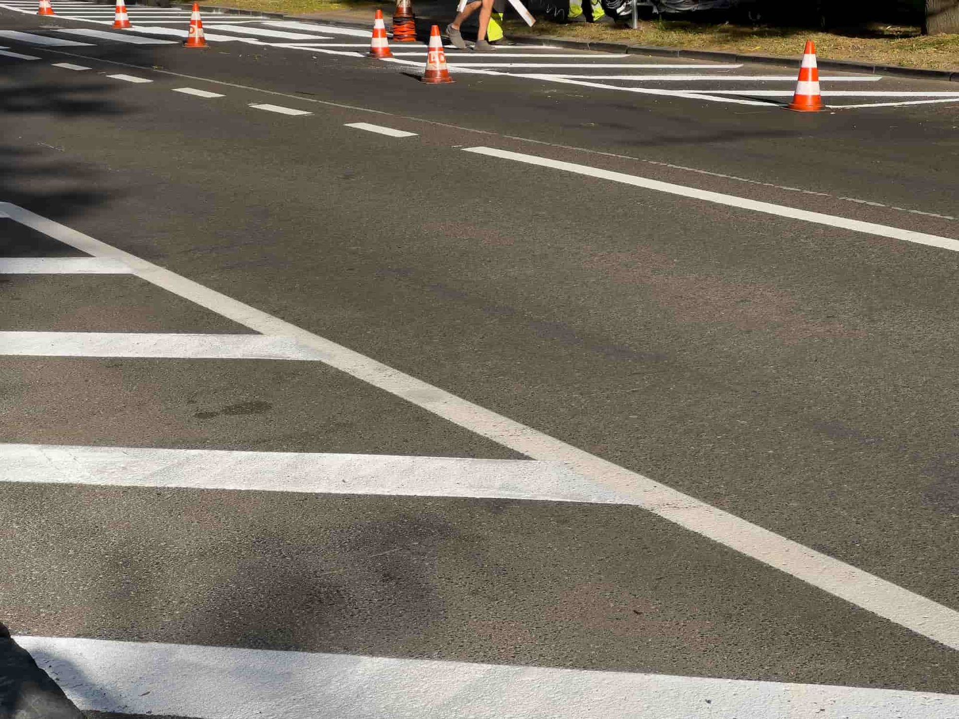 Road with white lane markings and orange traffic cones; person running in the distance.