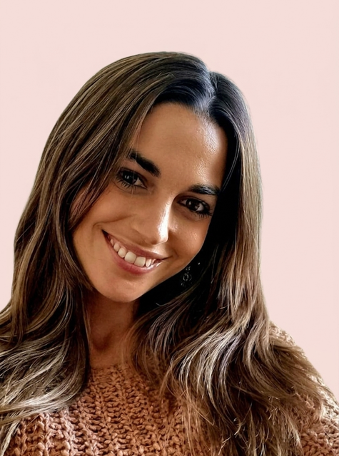 Mujer sonriente con cabello castaño largo que lleva un suéter marrón texturizado sobre un fondo claro.