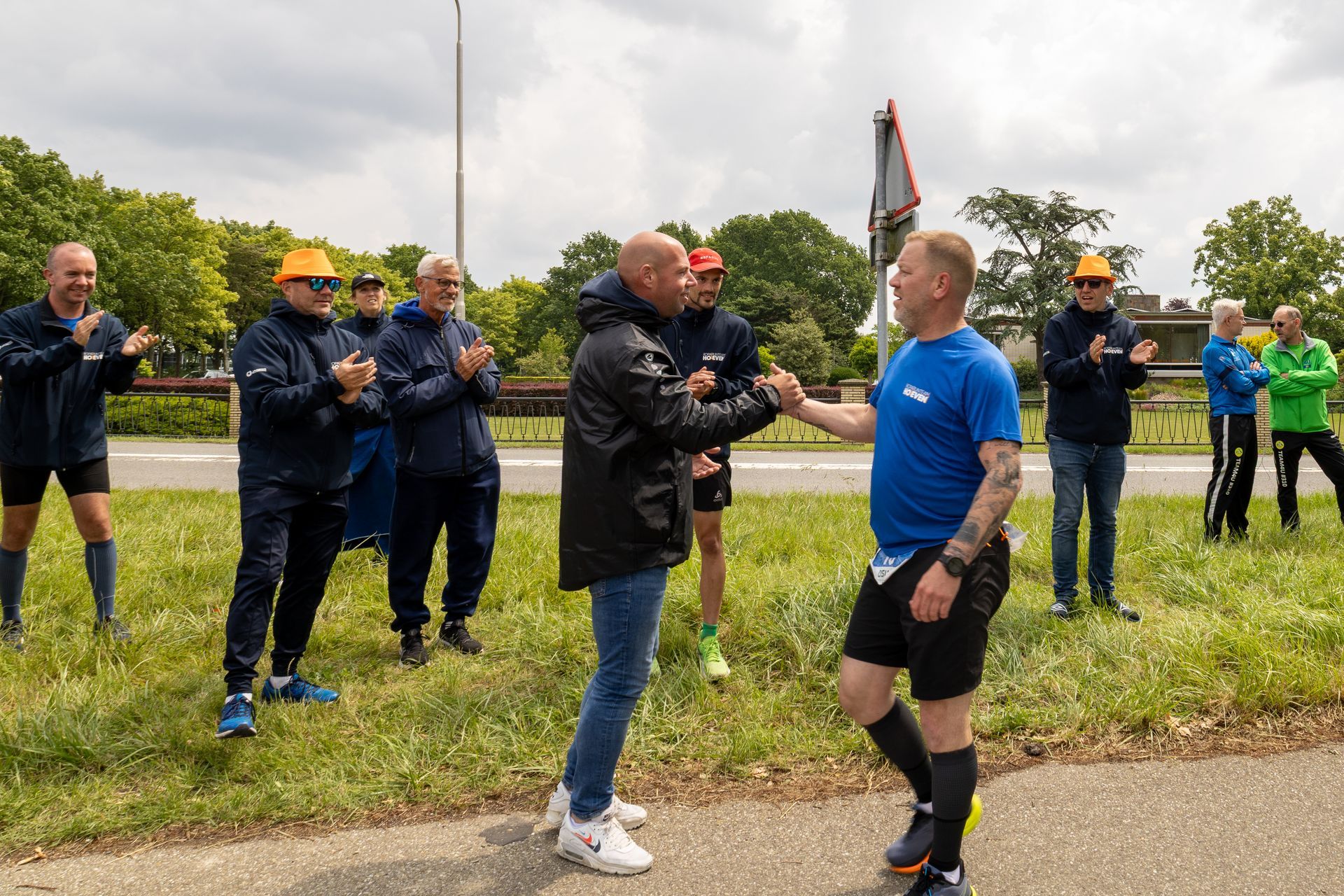 Mensen in outdoor sportkleding staan ​​langs een pad en applaudisseren wanneer twee mannen binnenkomen