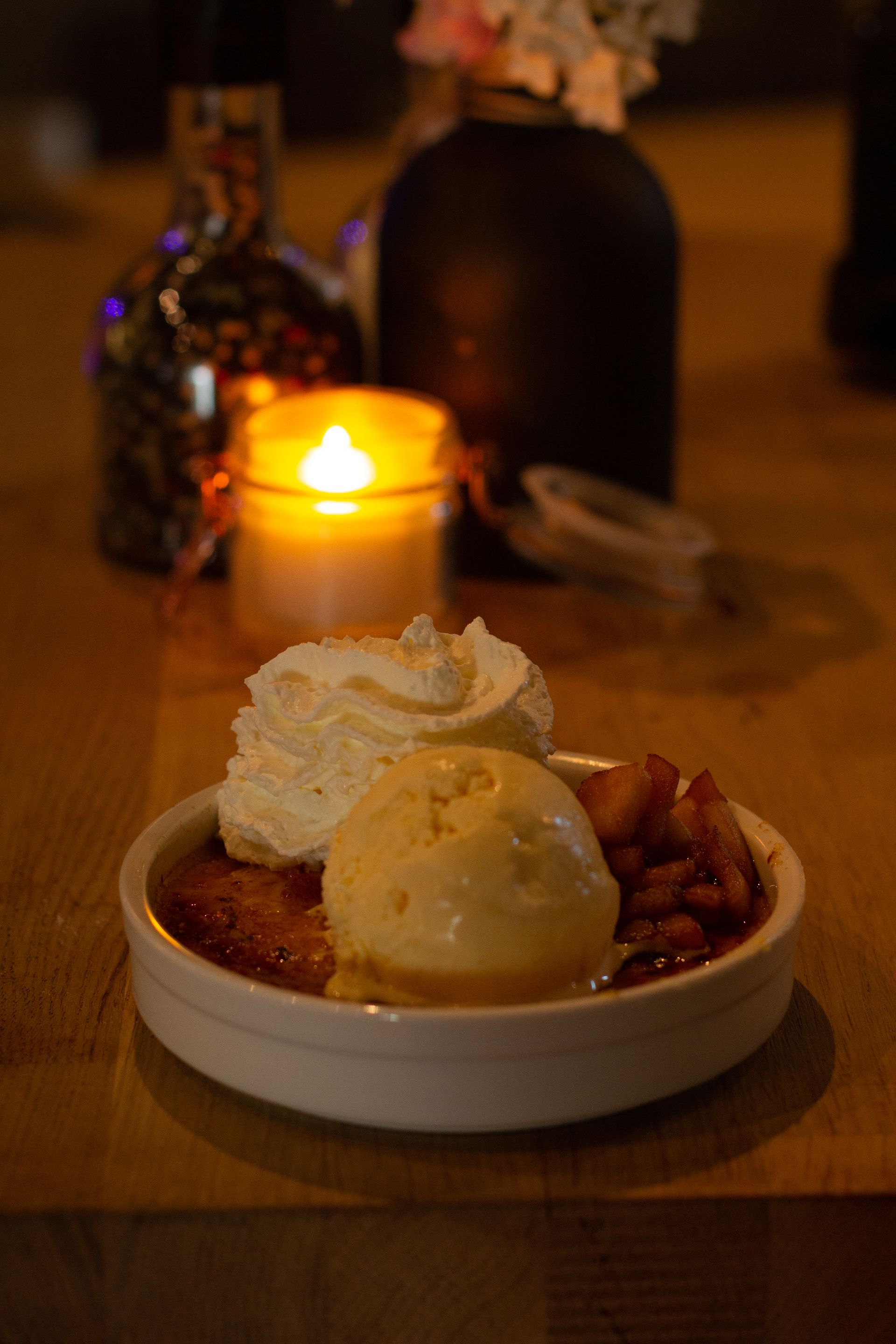 Een ijsdessert met slagroom op een klein bordje, verlicht door een kaars op een schemerige tafel.