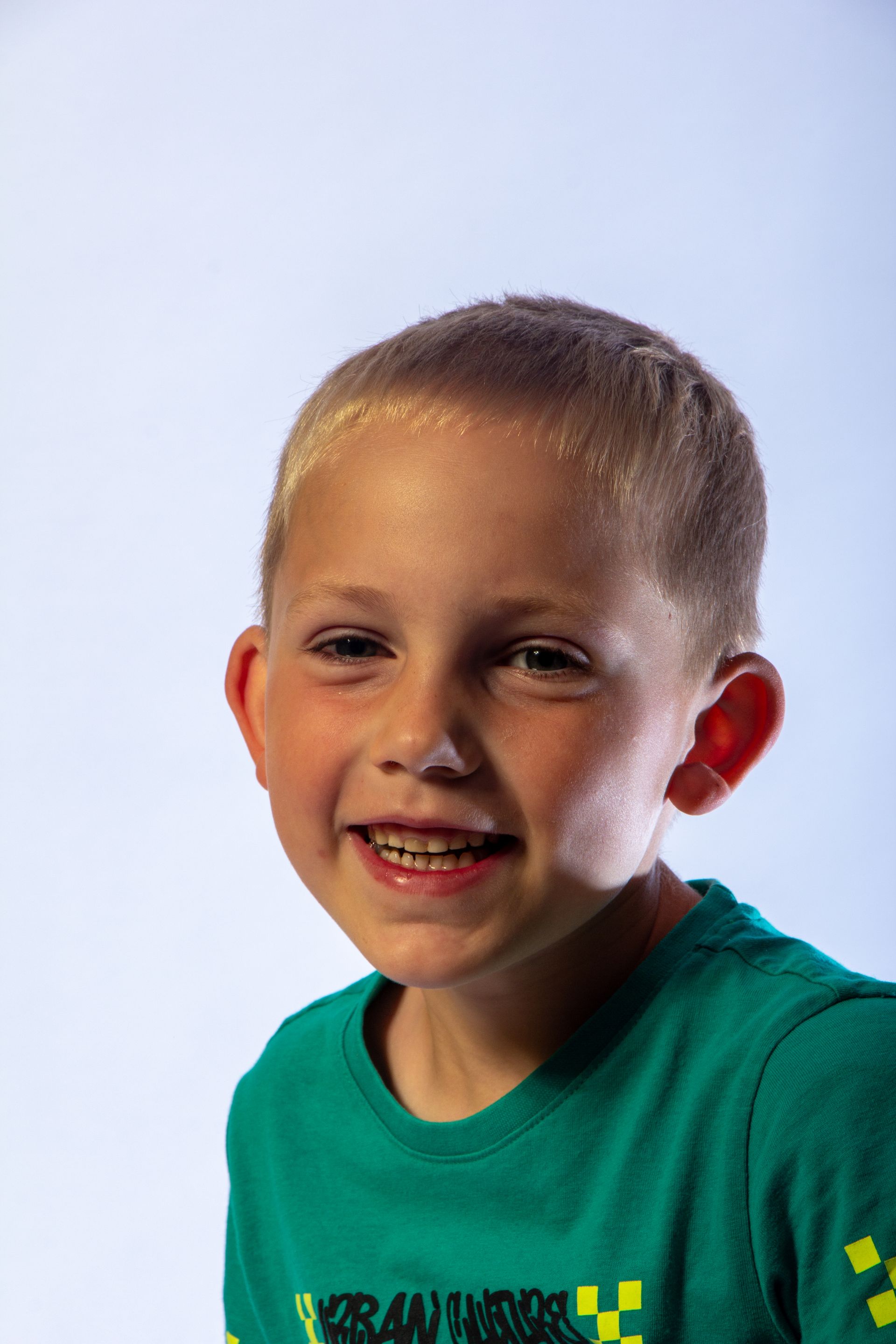 Lachend kind in een groen shirt tegen een lichtblauwe achtergrond