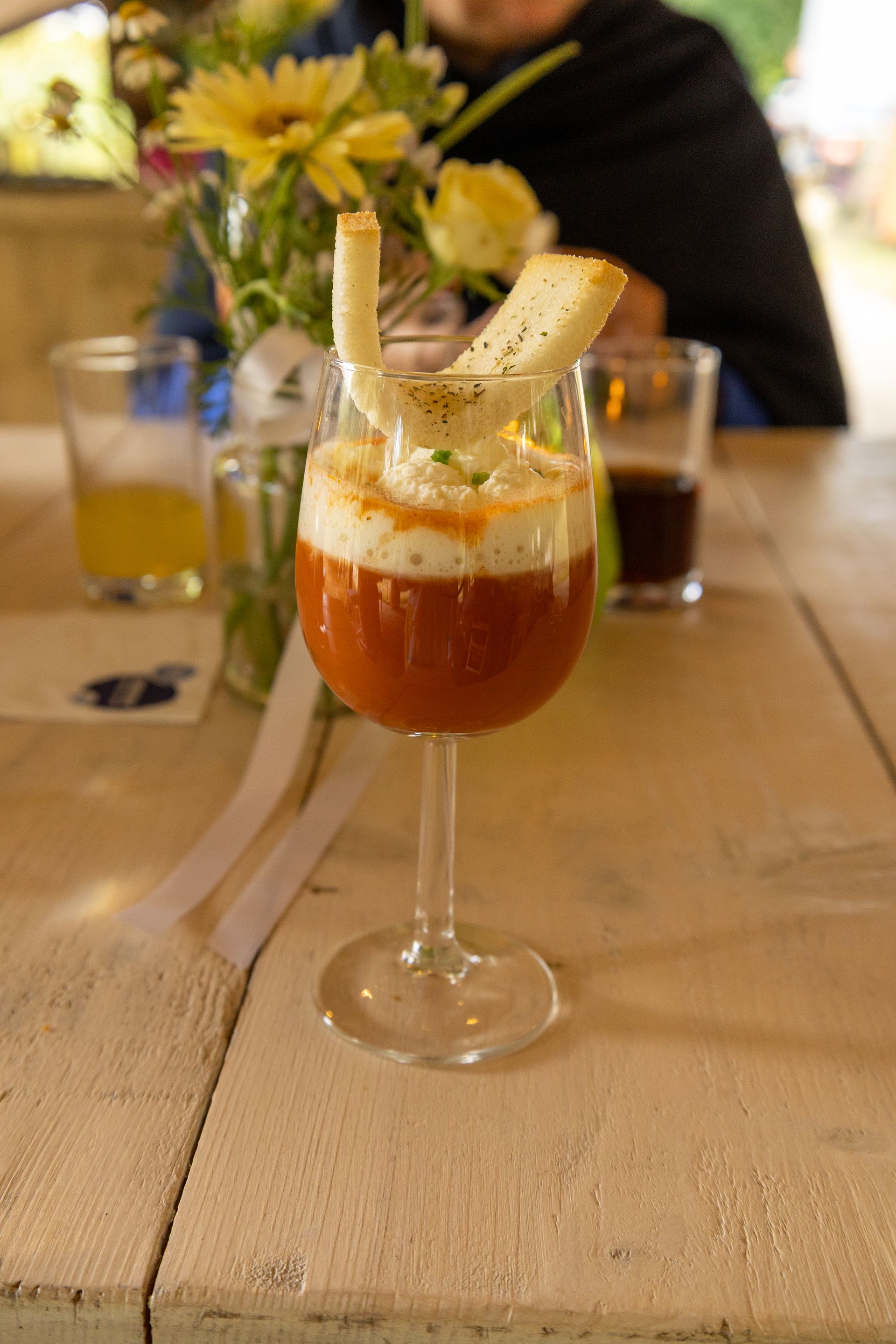 Een rode cocktail met een schijfje banaan en bloemen op een rustieke tafel in een restaurant.