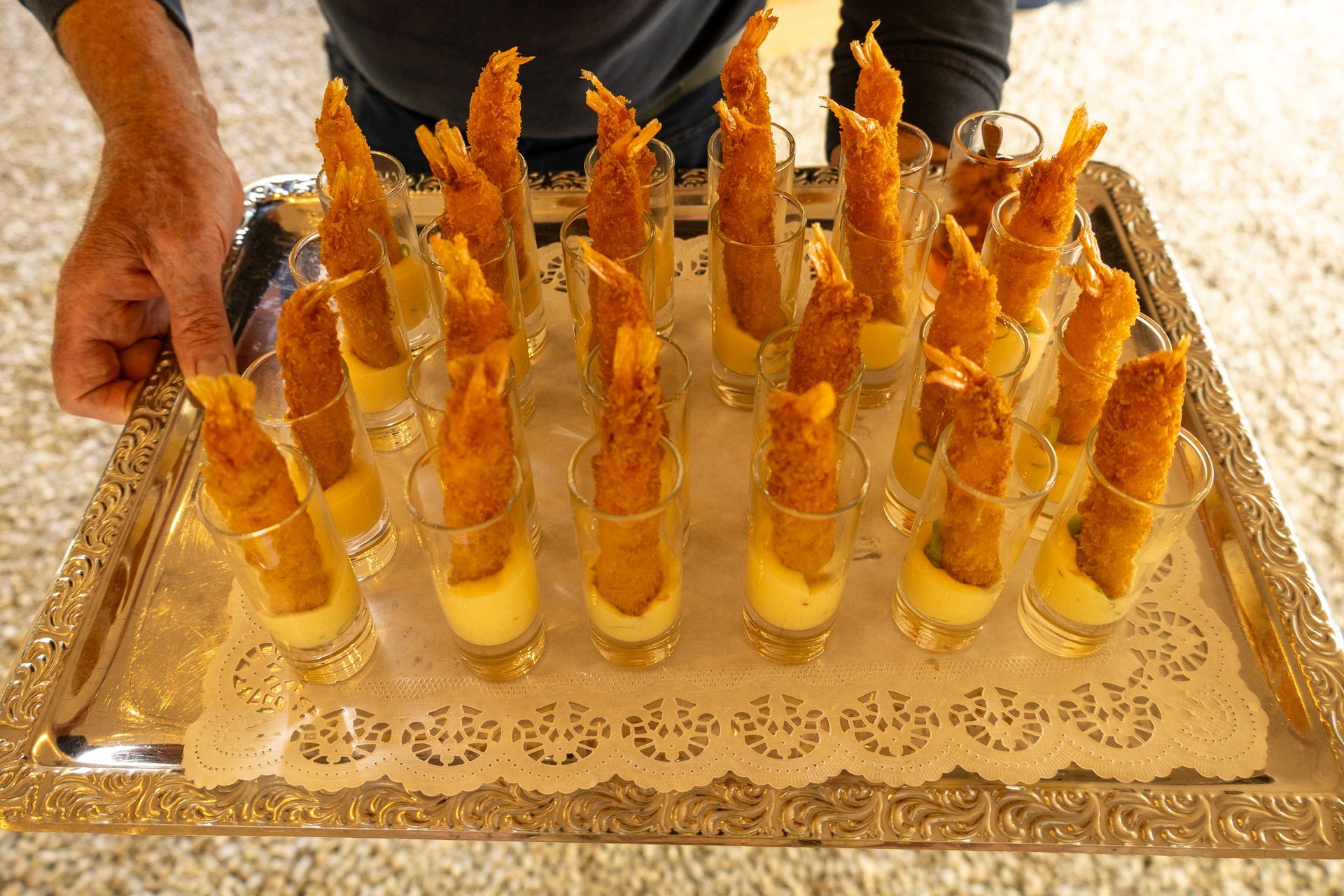 Een dienblad met doorzichtige bekertjes gevuld met gele dessert- en wafelhoorntjes, vastgehouden door een persoon.