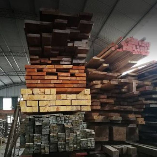 Montones de madera y tablones almacenados en un almacén bajo un alto techo metálico.