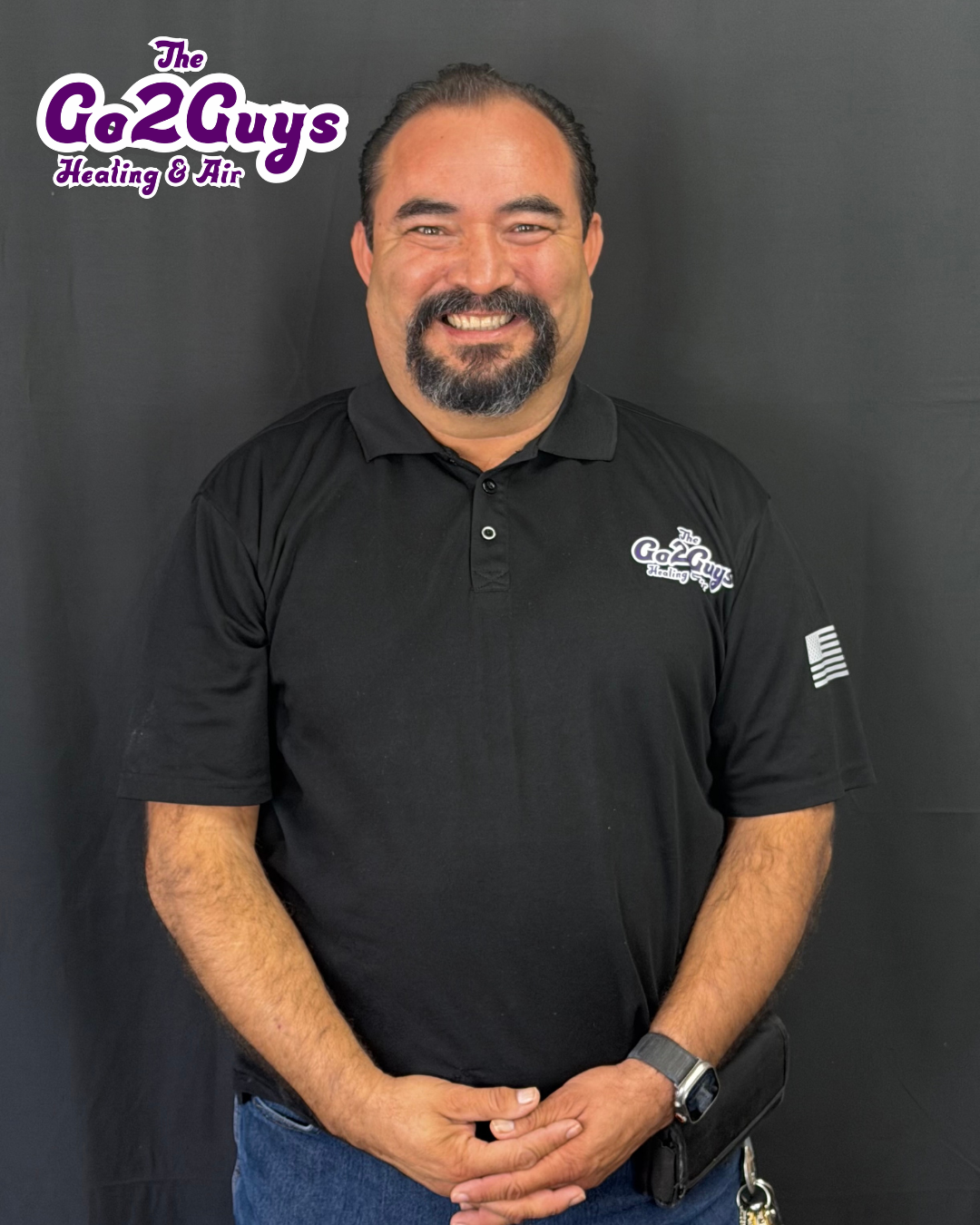 Smiling man in black polo shirt standing against a gray backdrop with Go2Guys logo