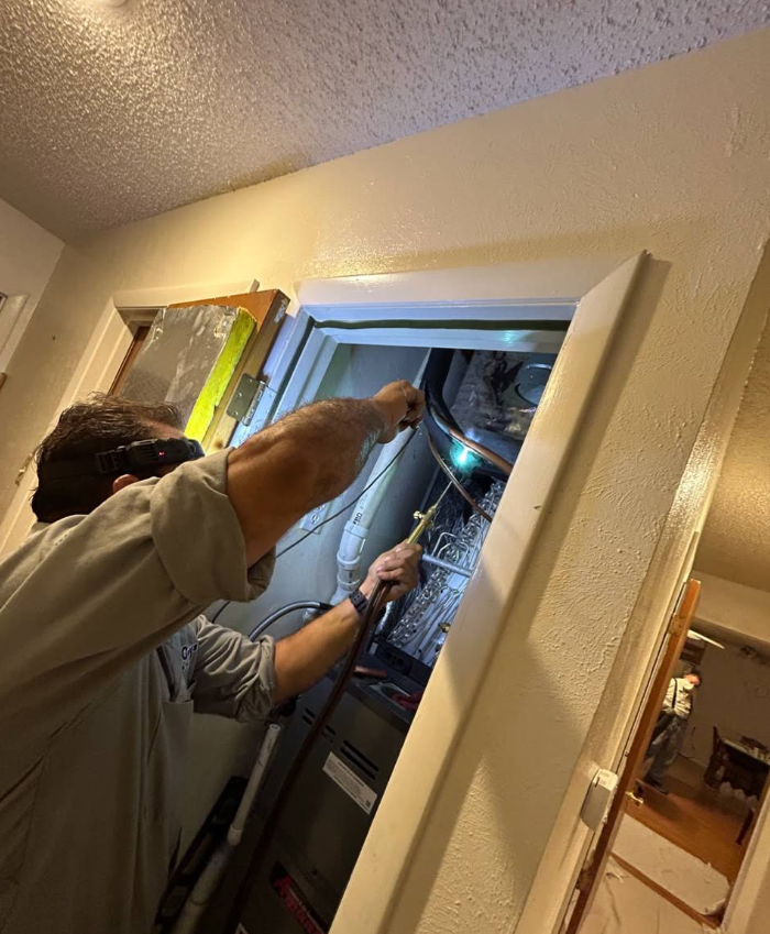 Technicians working on exposed wiring inside a home electrical panel in a hallway closet
