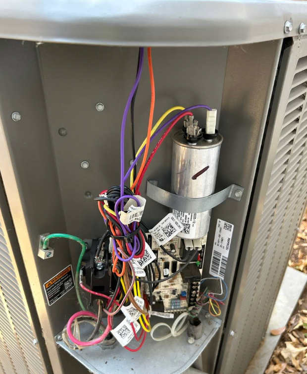 Open HVAC unit with exposed wiring, circuit boards, and a metal capacitor inside.