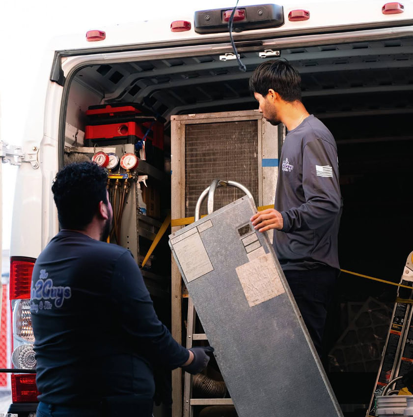 Two workers loading equipment into the back of an ambulance-style truck