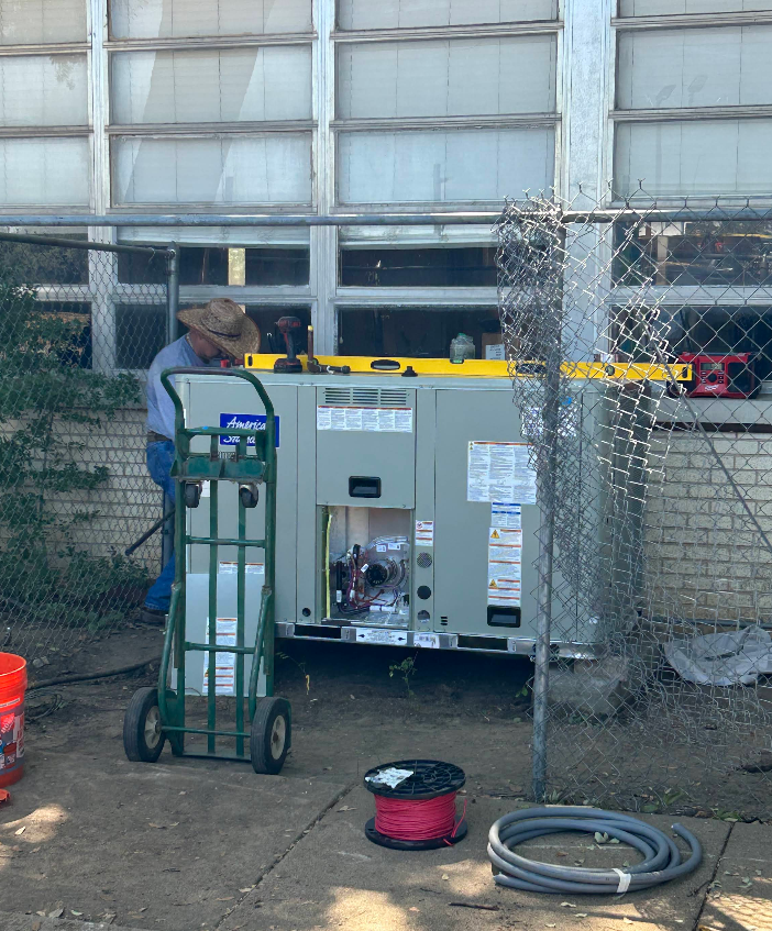 Outdoor industrial generator beside a chain-link fence, with hoses and a worker nearby.