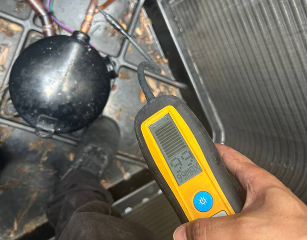 Handheld digital meter checking a black tank or pipe beside a metal grate floor