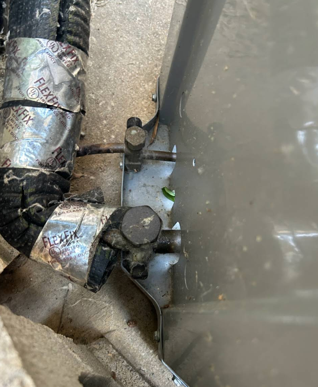 Insulated pipes and a valve beside a gray wall, with water or condensation around them