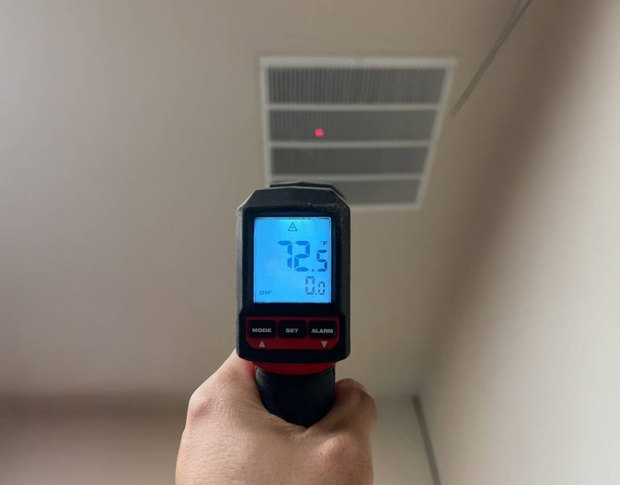 Handheld infrared thermometer aimed at a ceiling vent, showing 22.5°C on its blue display