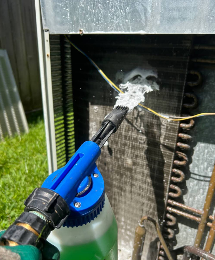 Garden hose spraying water onto an air conditioner coil outdoors