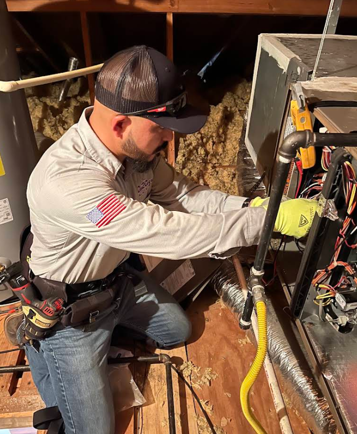 Technician in beige shirt works inside a furnace, adjusting wiring in a mechanical room.