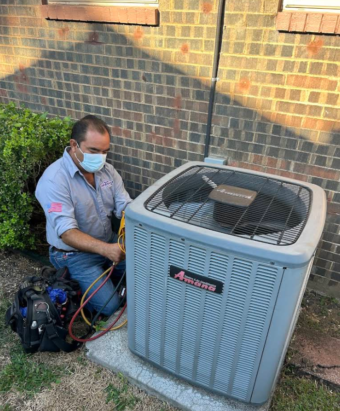 Technician servicing a rooftop HVAC unit beside a brick wall, with tools and gauges attached