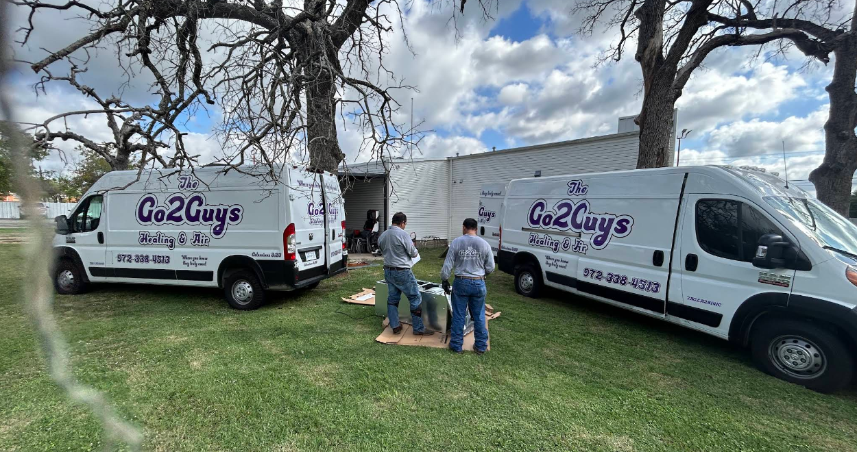 Two white business vans parked on grass with three people between them under a cloudy sky.