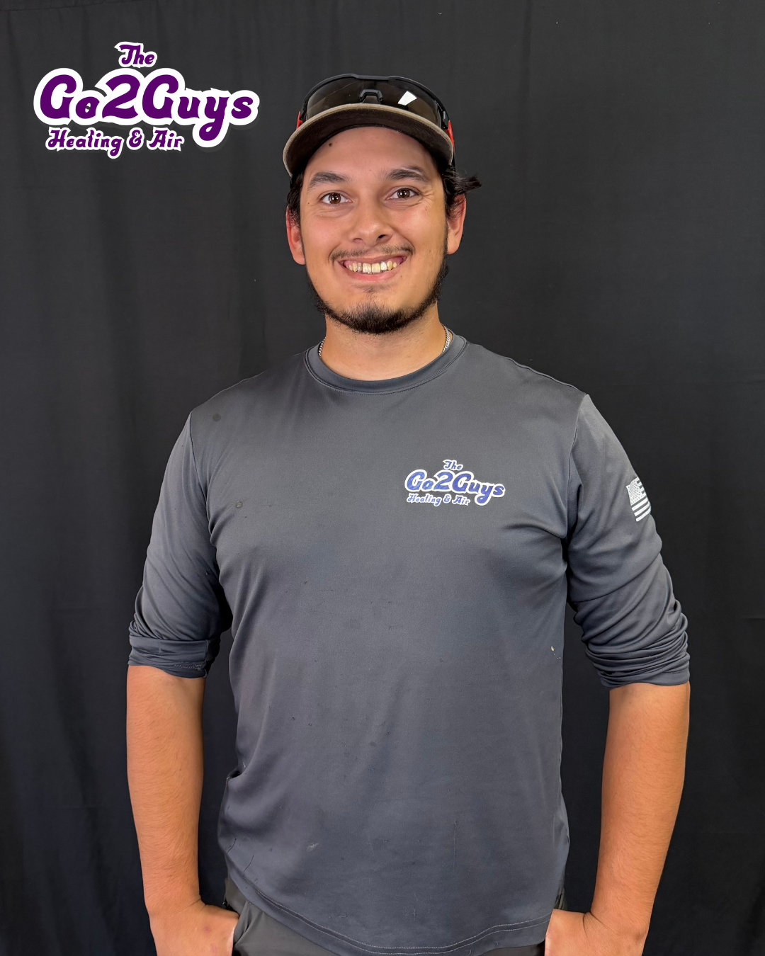 Man in gray long-sleeve shirt and black cap smiling against a dark backdrop, with Go2Guys Plumbing Co. logo.