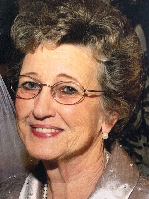 A woman wearing glasses and a pearl necklace is smiling for the camera.