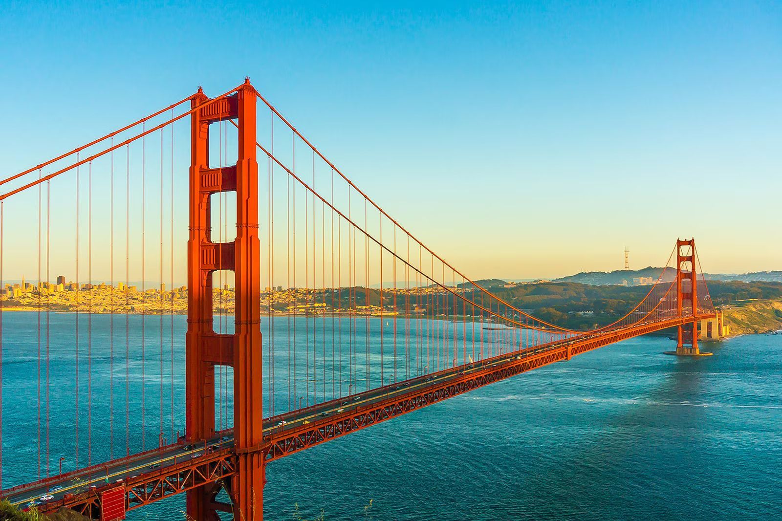 Golden Gate Bridge spanning blue water at sunset, with the city skyline in the distance.