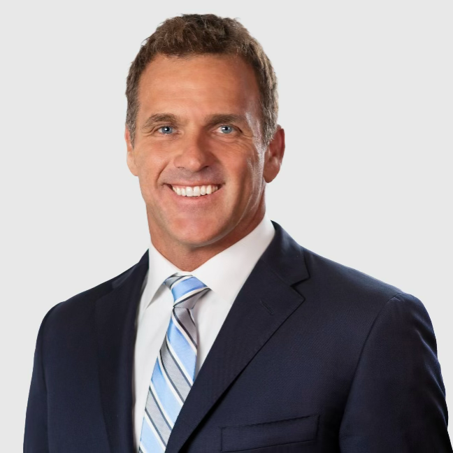 Professional man in navy suit and striped tie, smiling against a light background