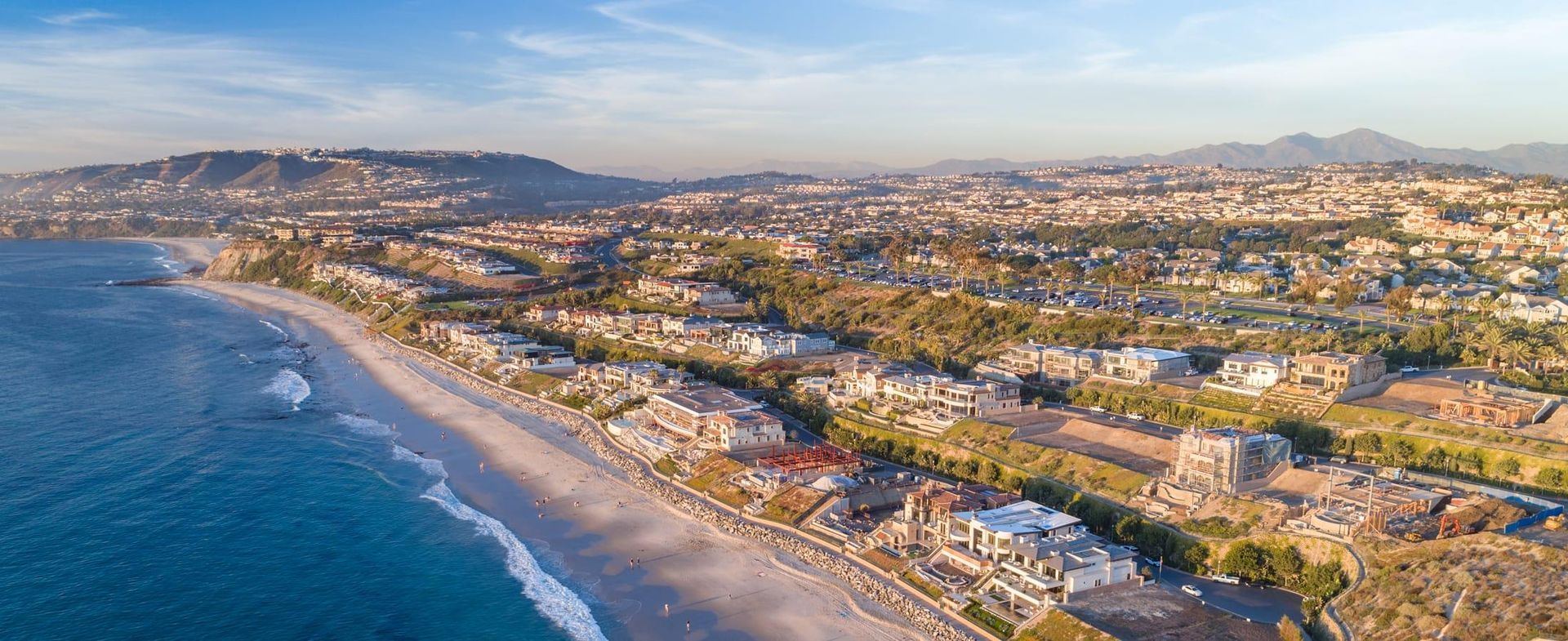 Aerial view of a coastal city with a wide beach, blue ocean, and hills in the distance