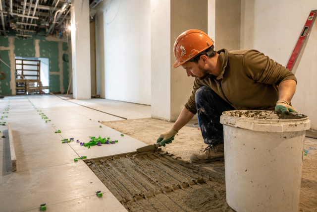 Worker in orange hard hat spreading wet concrete in an unfinished hallway