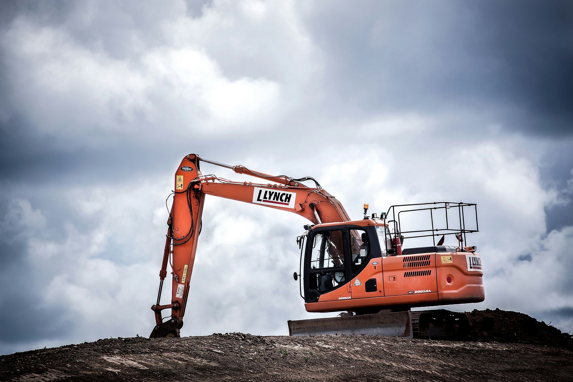 Orange excavator on a dirt mound under a cloudy sky