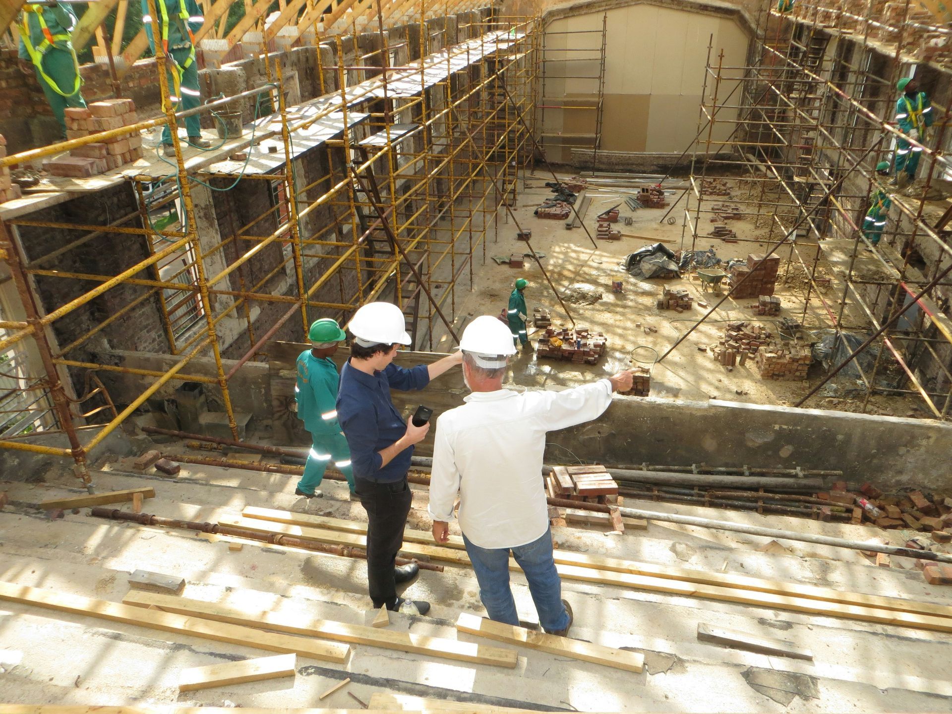 Construction workers in hard hats observing a large excavation with scaffolding and debris at a site