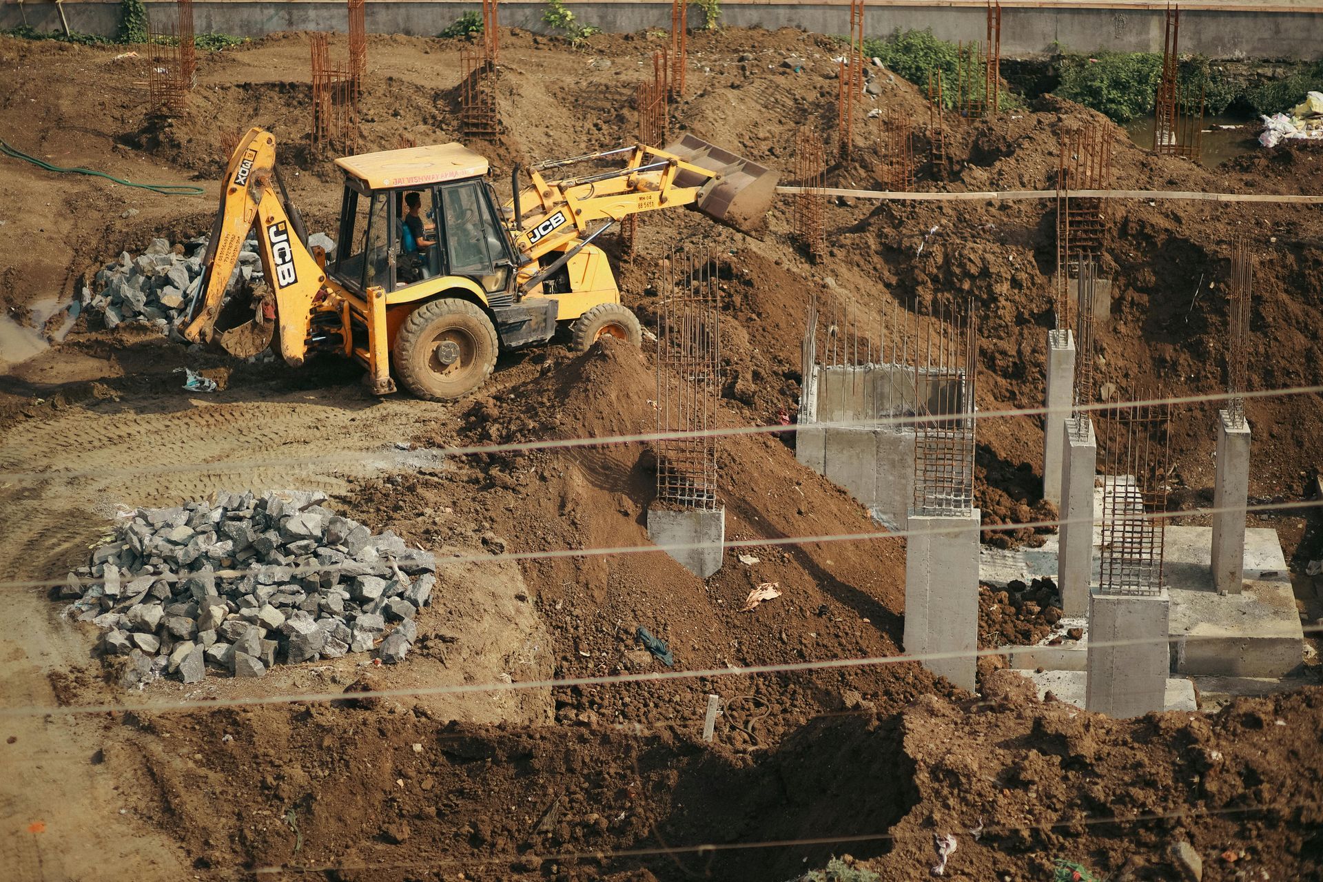 Yellow backhoe excavator working at a construction site with dirt piles and concrete foundations
