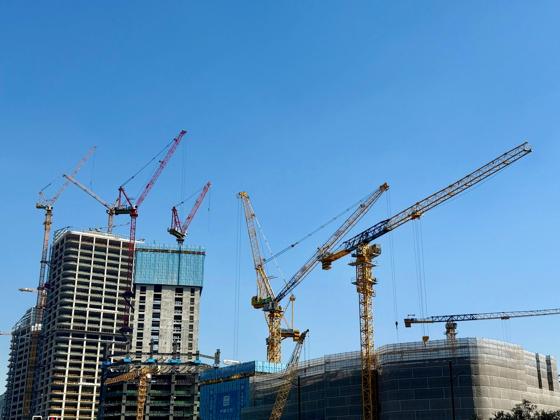 Construction site with tall cranes and partially built high-rise buildings under a clear blue sky