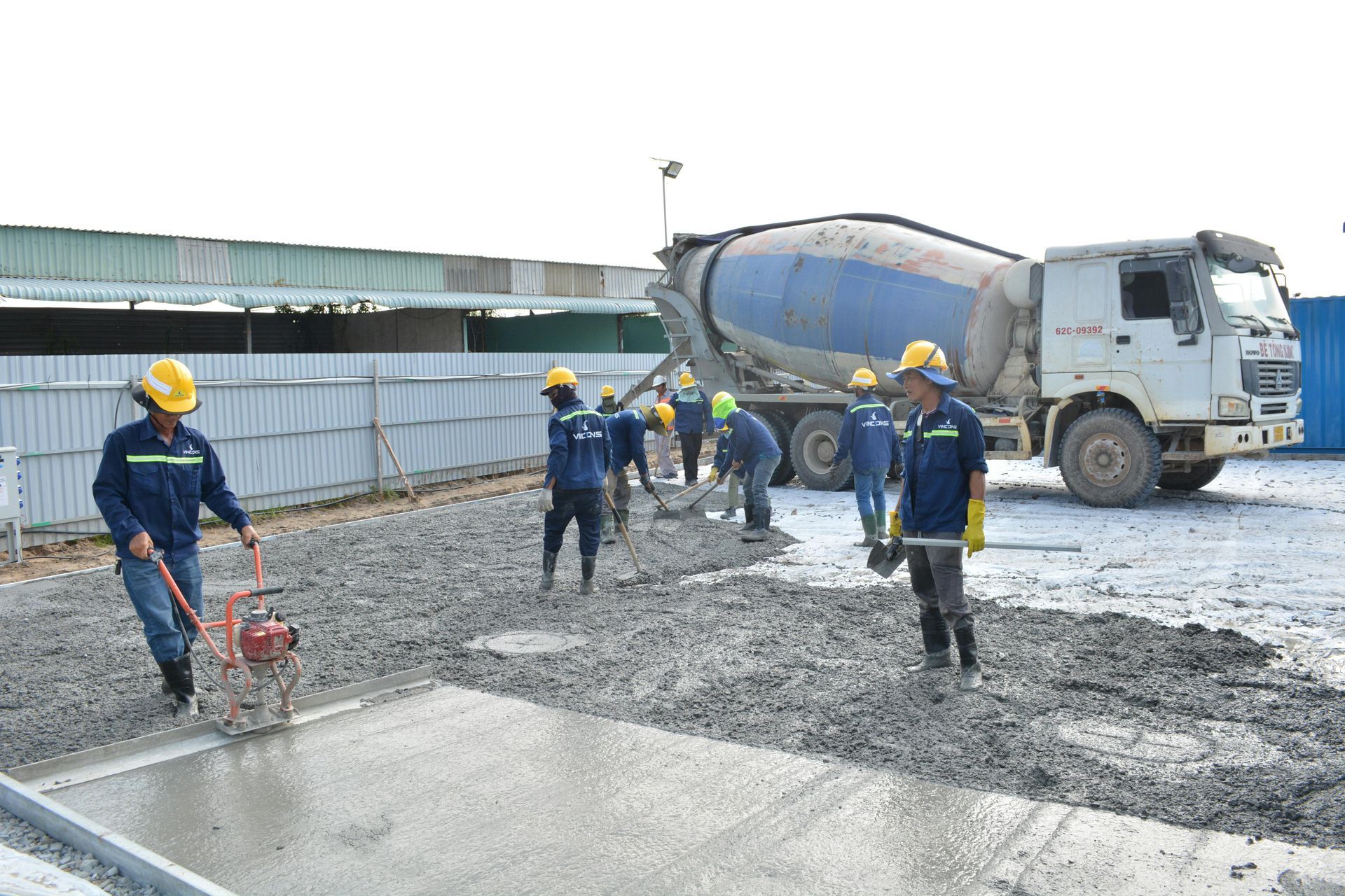 Construction workers paving a road beside a cement mixer truck, wearing hard hats and safety gear.