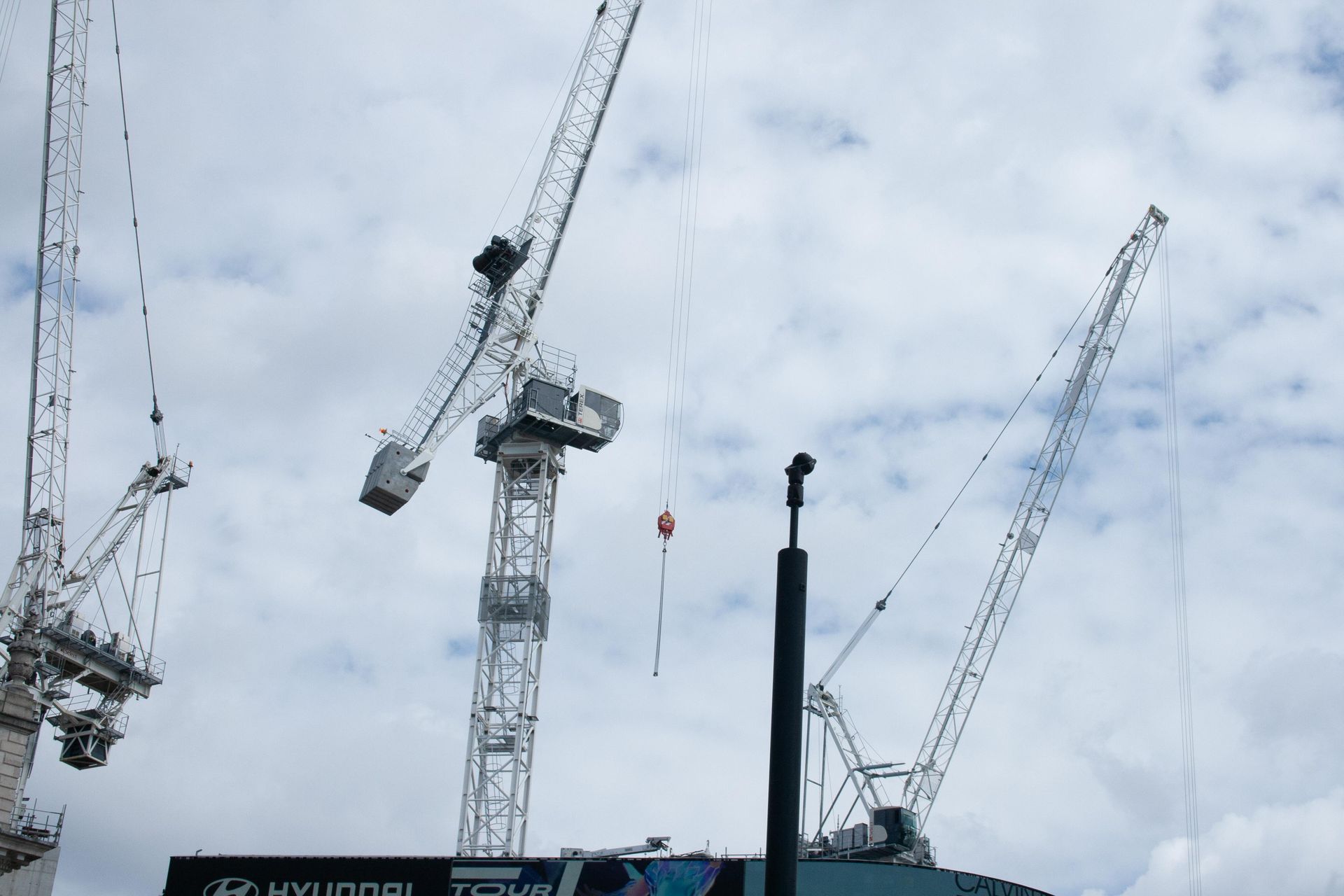 Several construction cranes against a cloudy sky at a building site
