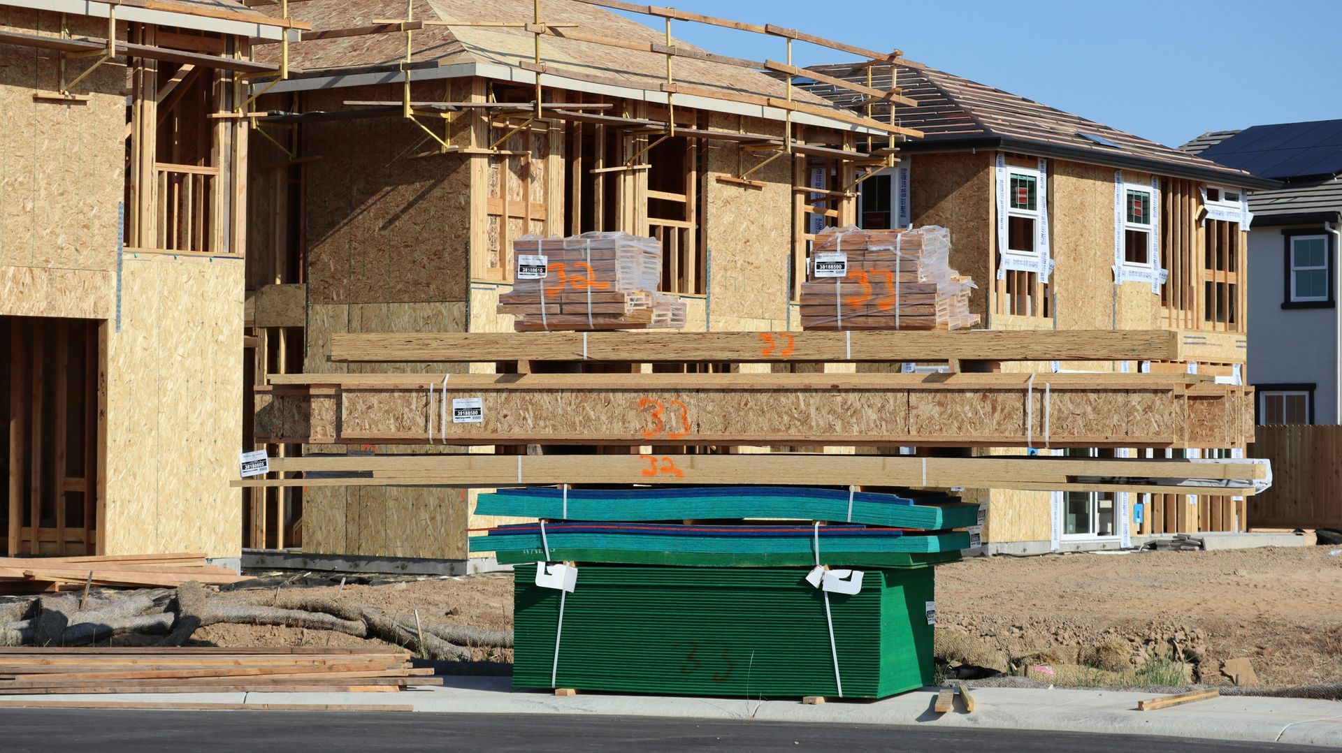Partially built house under construction with wood framing, windows, and a green dumpster in front