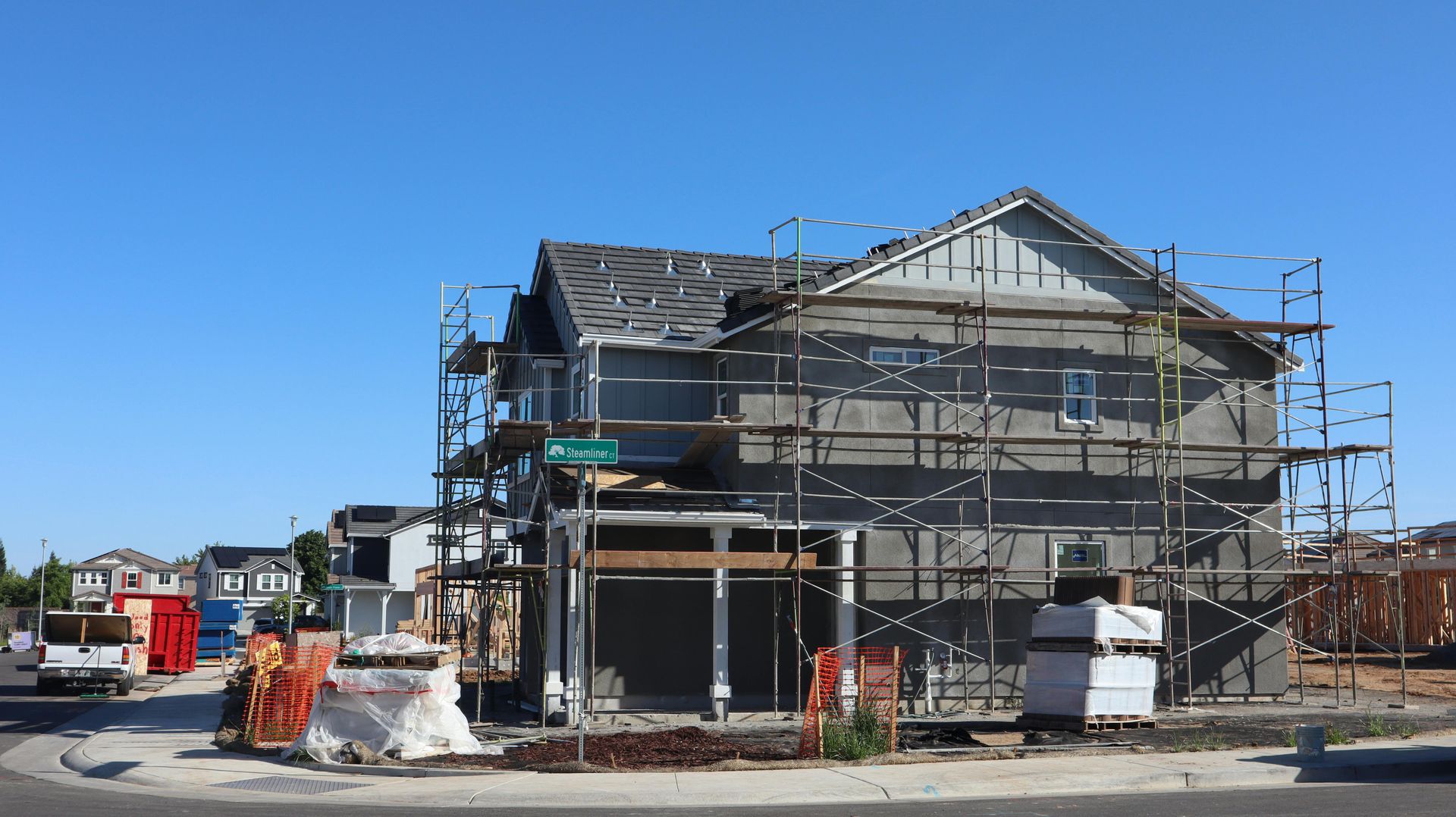 House under construction with scaffolding, exposed framing, and building materials on a clear day