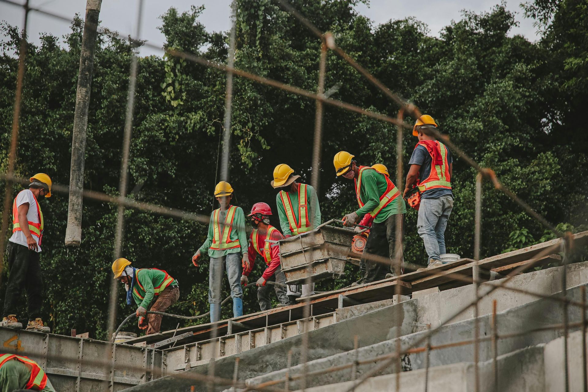 Construction workers in yellow helmets on scaffolding at a building site, carrying materials.