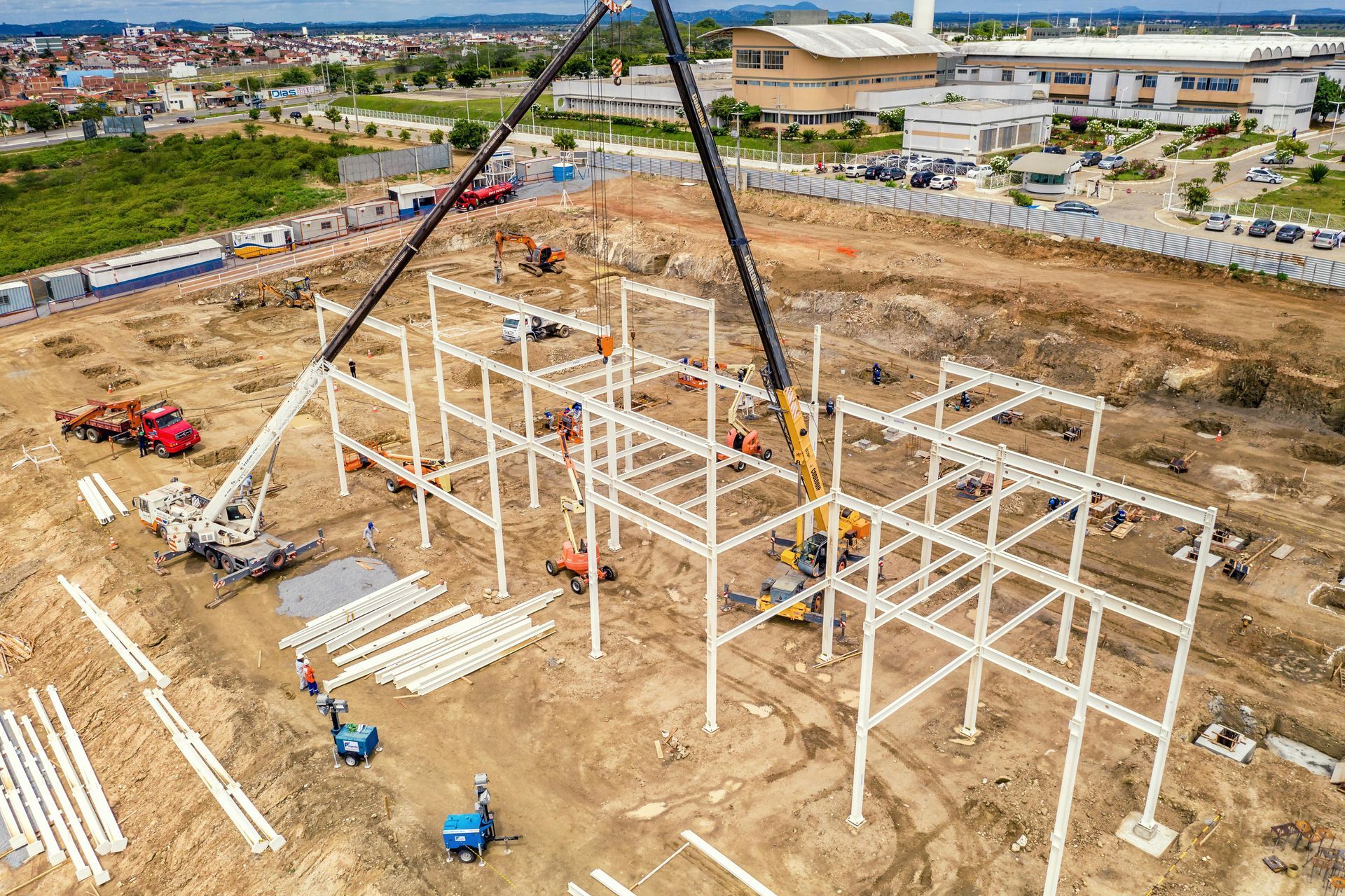 Construction site with a steel building frame, cranes, and workers on a dirt lot