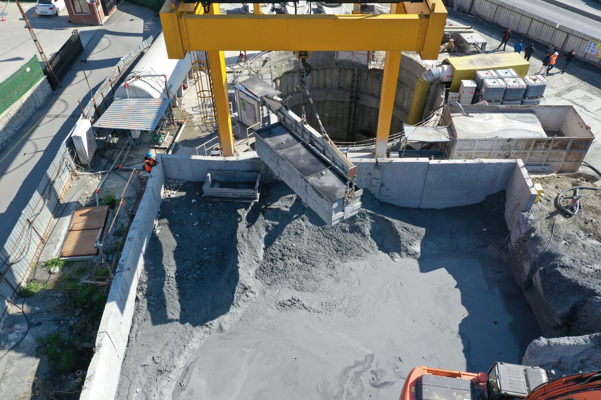 Construction site with concrete excavation and a yellow crane lifting debris beside retaining walls