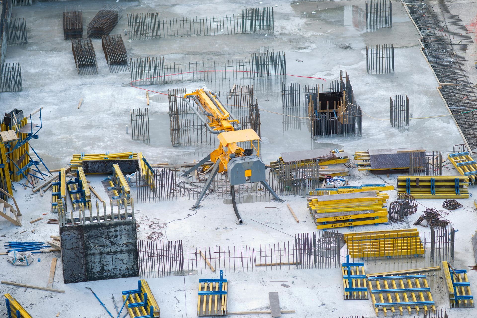 Construction site with yellow excavator amid concrete foundations, rebar, and materials in snow