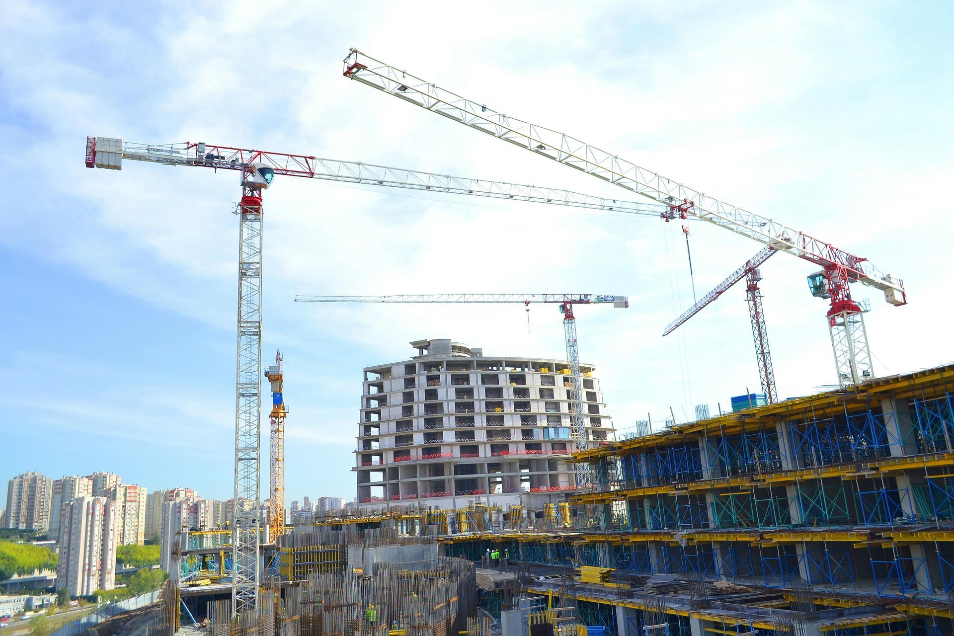 Construction site with tall cranes and a partially built high-rise under a blue sky