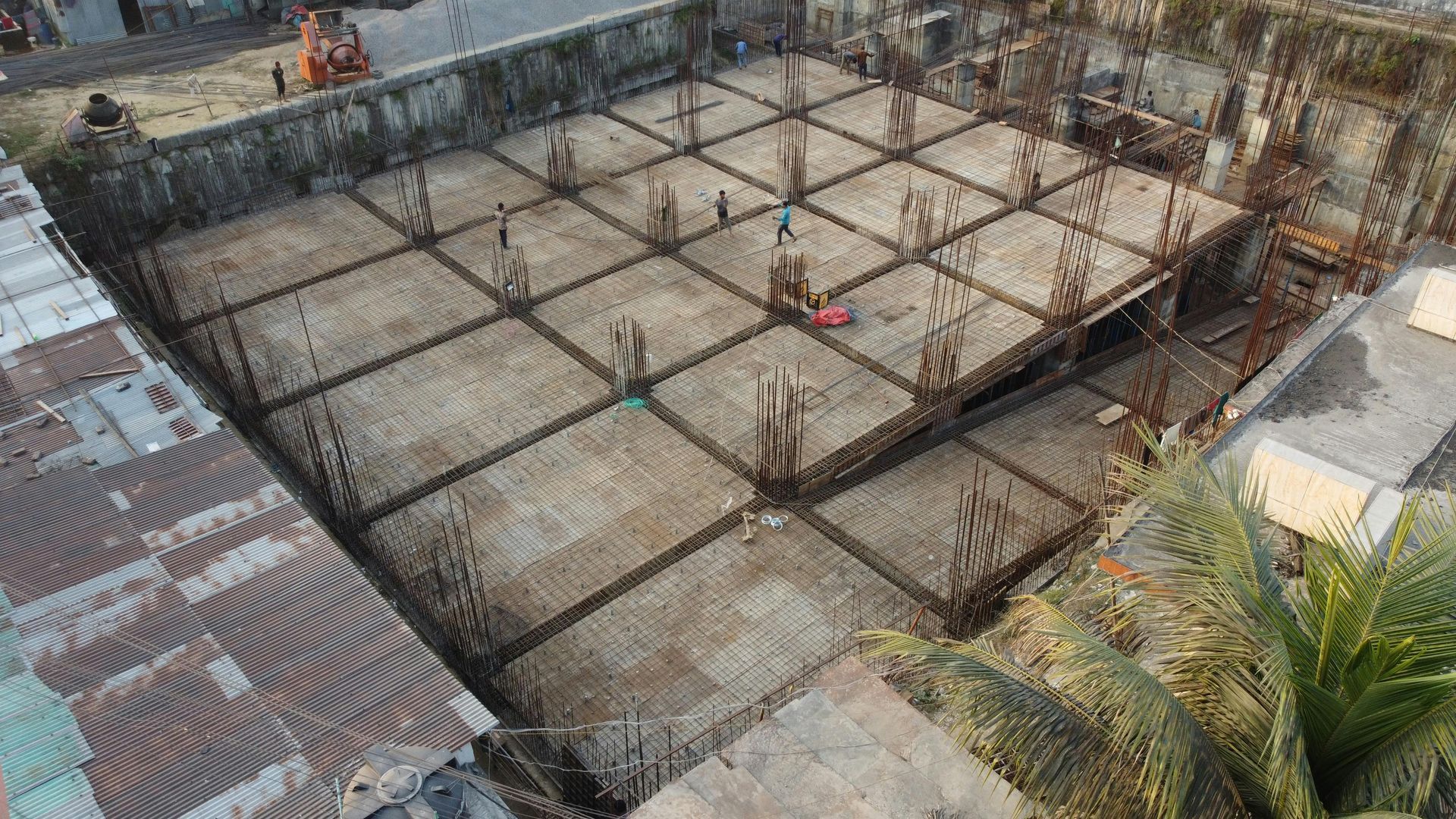 Construction site with a large reinforced concrete foundation grid and workers around the perimeter