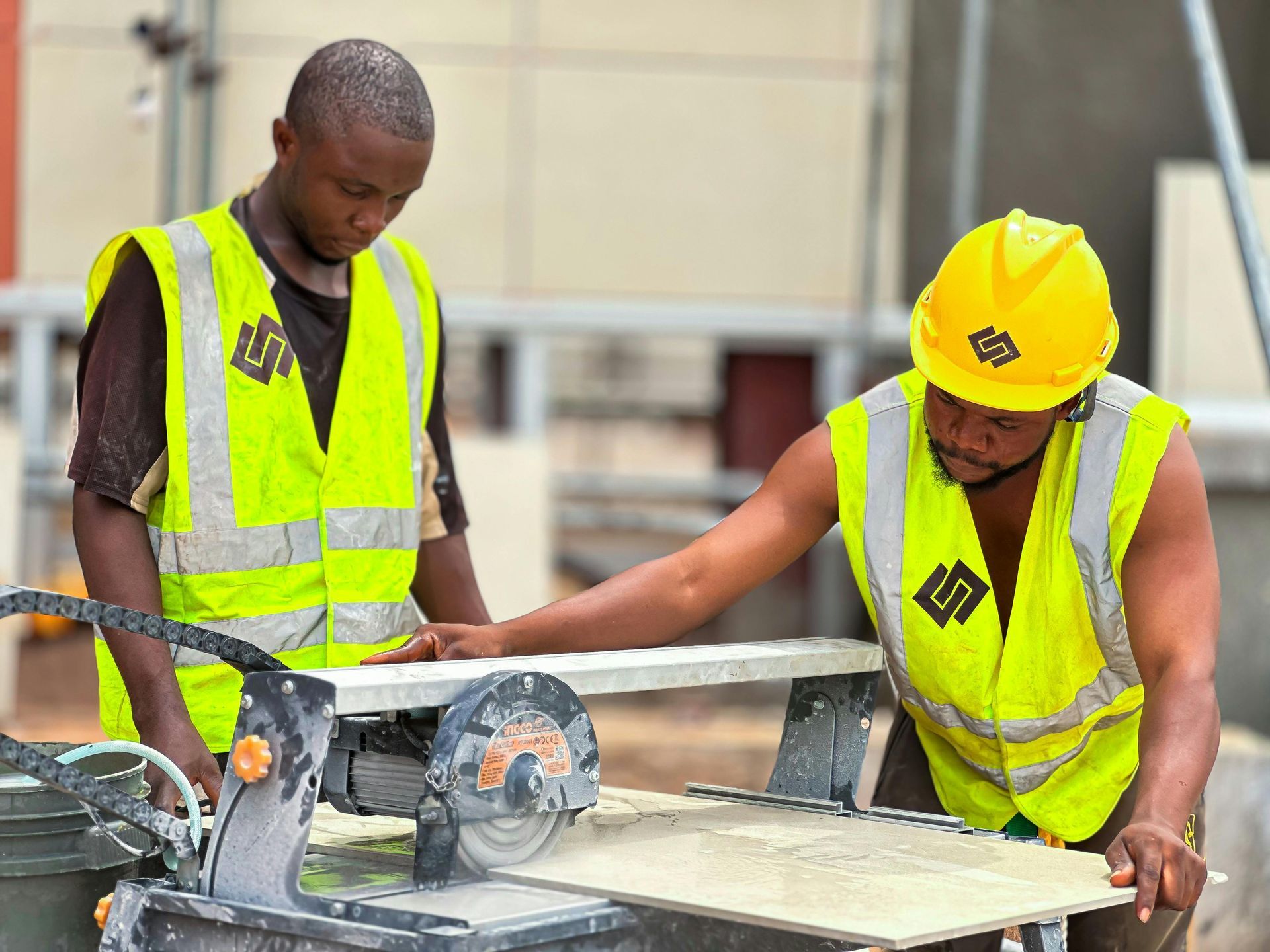 Two construction workers in yellow safety vests and hard hats measuring wood with a circular saw on a worksite