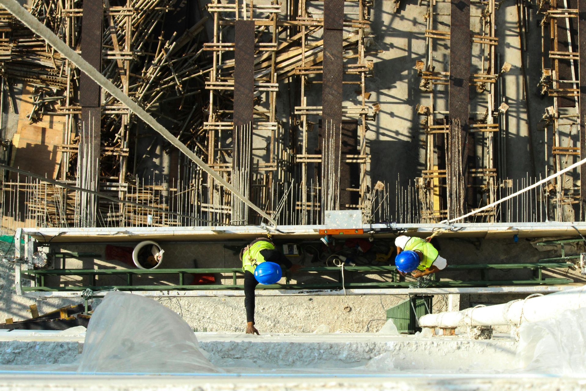 Two workers in safety gear inspect a pipe at a construction site with scaffolding behind them.